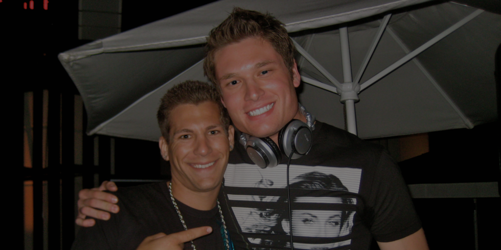 Host A Fashion Show Two young men smile at the camera; one wears a necklace and points, while the other has headphones around his neck and a graphic t-shirt. An outdoor umbrella is in the background.