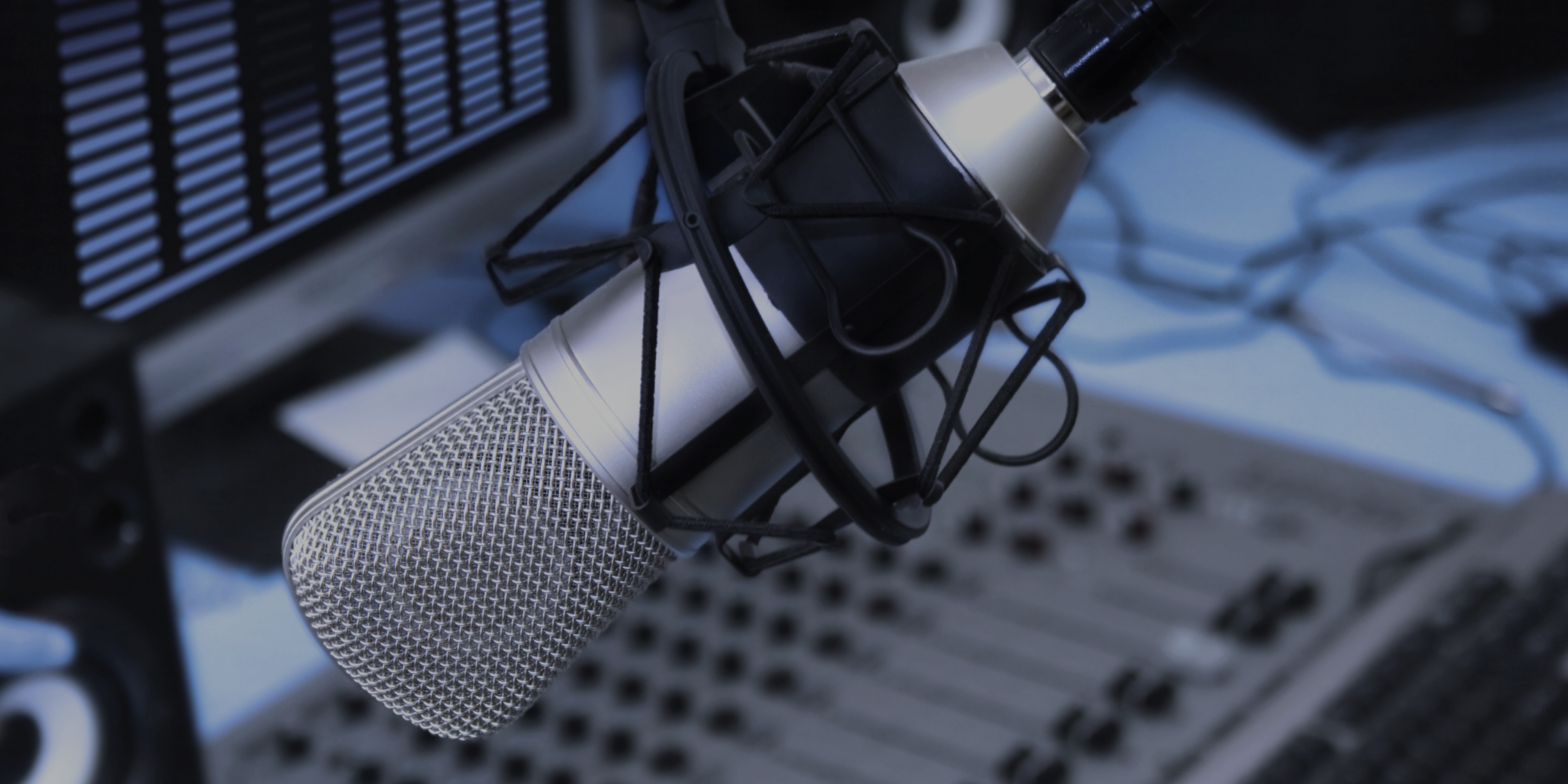 A close-up of a studio microphone with a pop filter, positioned in front of an audio mixing console.
