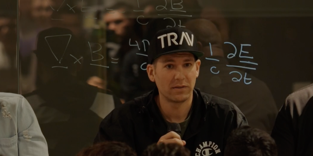 Boost Your Career with These 3 Simple Personal Branding Strategies A man wearing a black "TRN" cap speaks into a microphone in front of a glass wall with mathematical equations written on it.