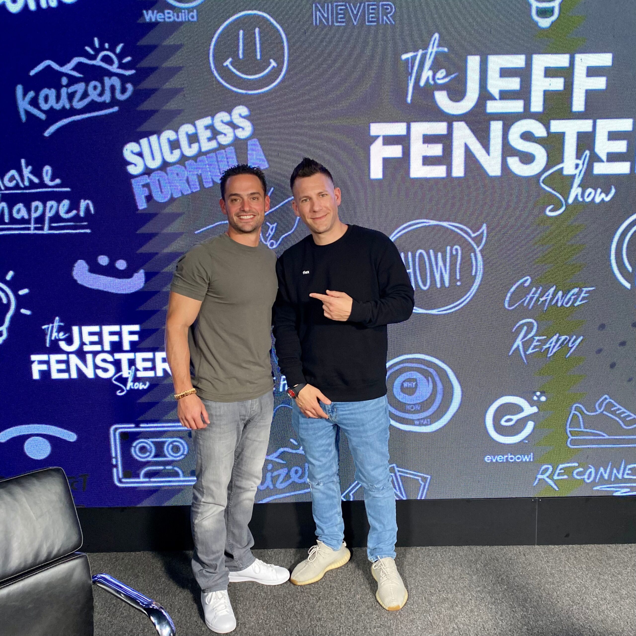 Two men stand in front of a blue backdrop featuring "The Jeff Fenster Show" and various motivational phrases and graphics.